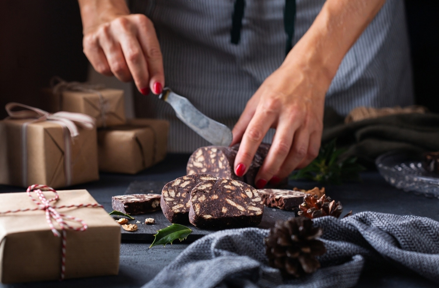 Hands slicing Not-A-Salami beside hand-wrapped gift boxes